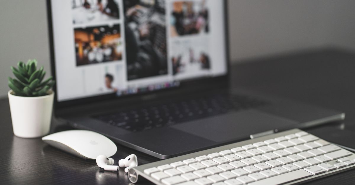 A sleek modern workspace featuring a laptop, keyboard, mouse, AirPods, and a small plant.