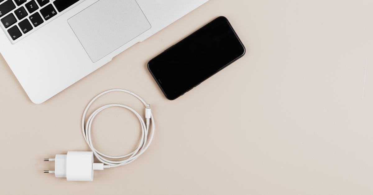Flat lay of a laptop, smartphone, and charger on a beige background showcasing modern technology essentials.